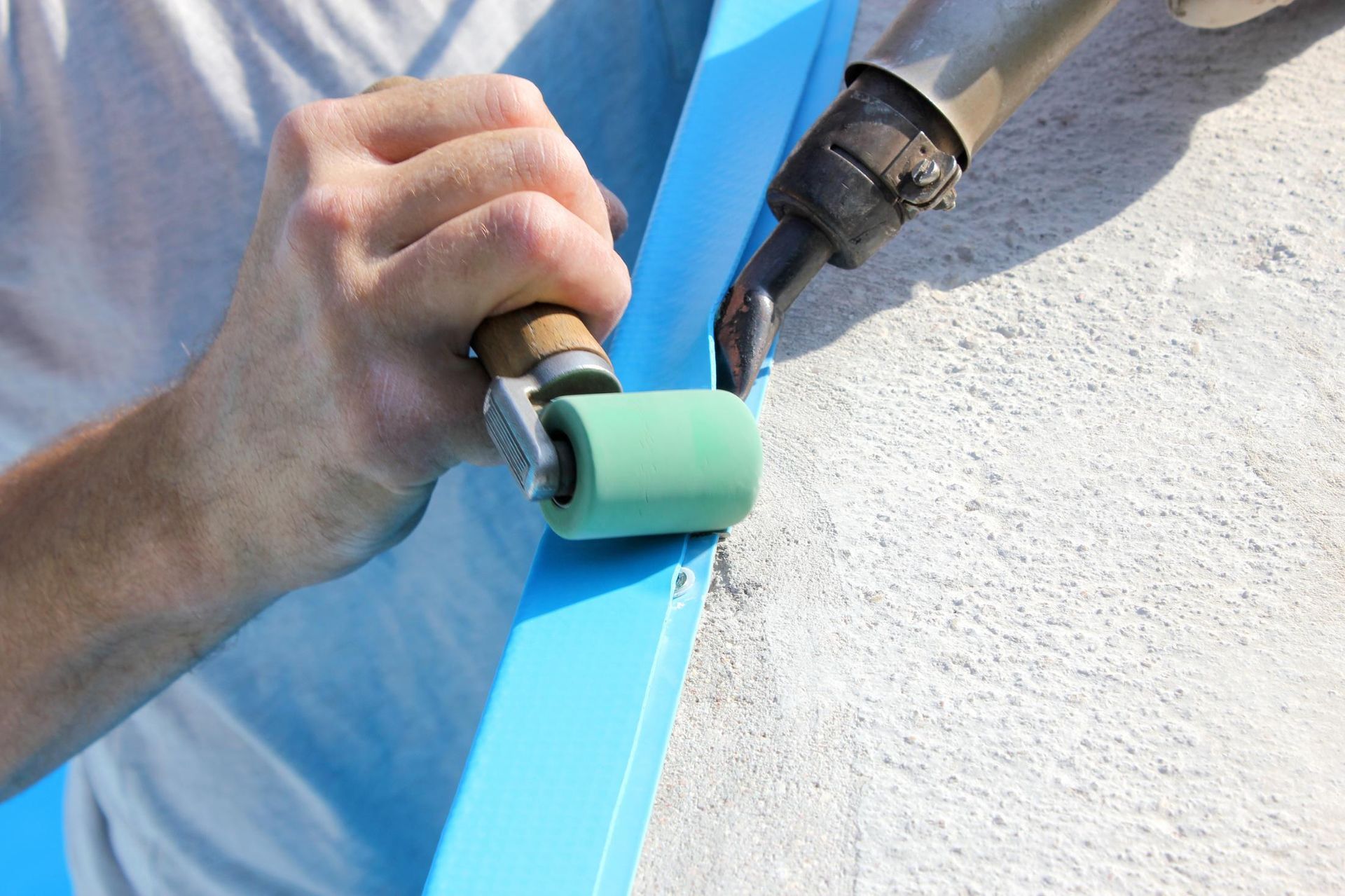 Hand painting a blue trim edge with a small green roller beside a white wall