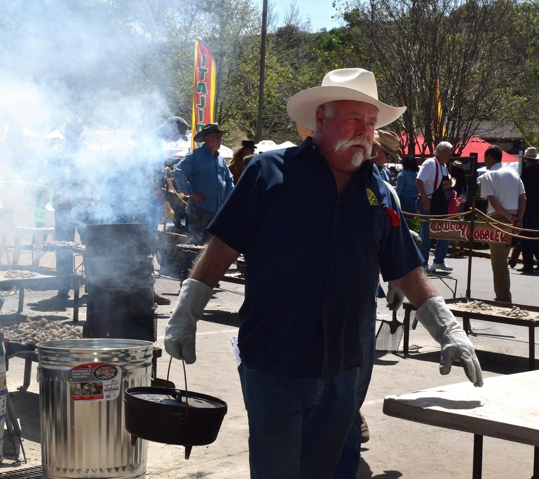 man in shirt wearing white gloves & a large brimmed white hat is cooking at a steaming pot