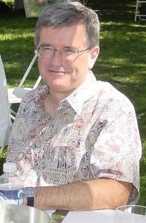 A man wearing glasses is sitting at a table with a cup of water.