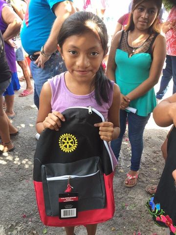 A little girl is holding a backpack with a rotary logo on it