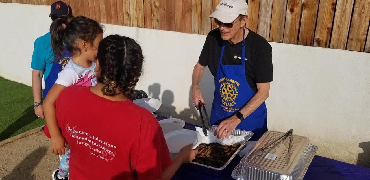 A man in a blue apron is serving food to a woman in a red shirt.
