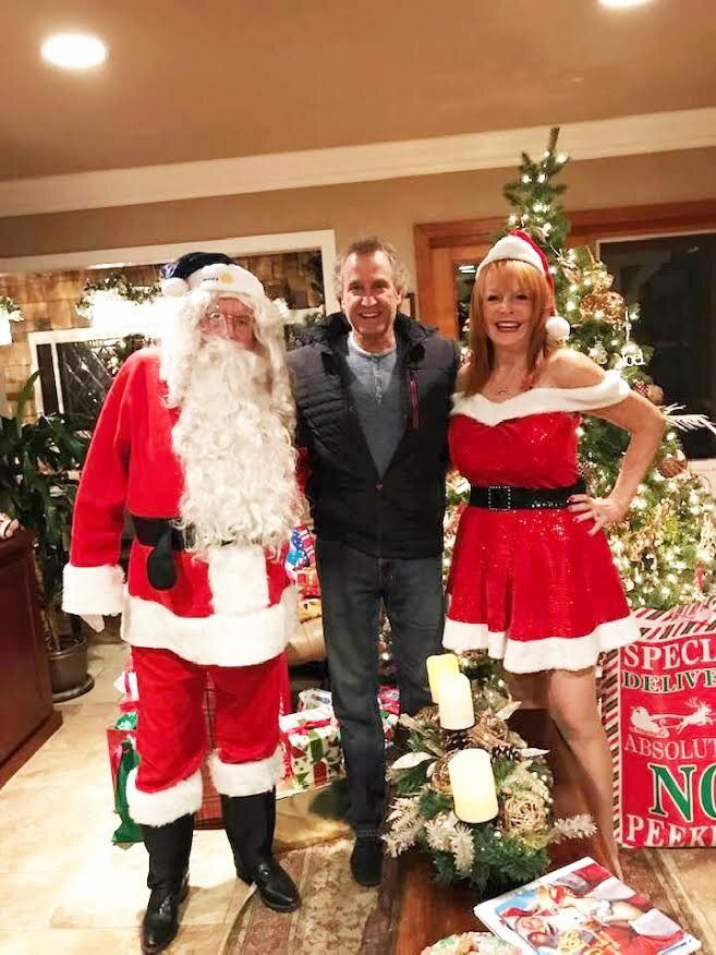 A man and two women dressed as santa claus are posing for a picture in front of a christmas tree.