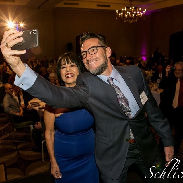 A man in a suit taking a selfie with a woman in a blue dress