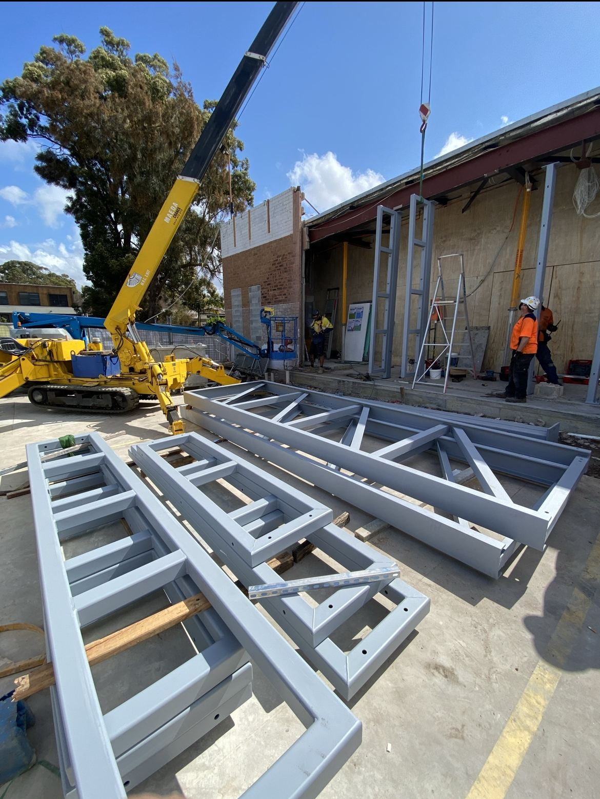 A crane is lifting a metal structure in front of a building.