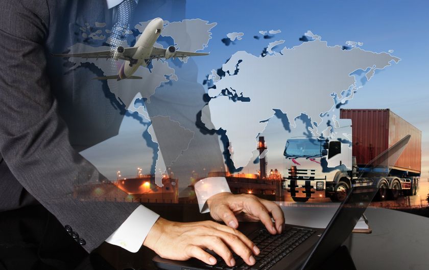 Airplane, truck and word map super imposed over a male office worker who is dressed in a suit and typing on a laptop
