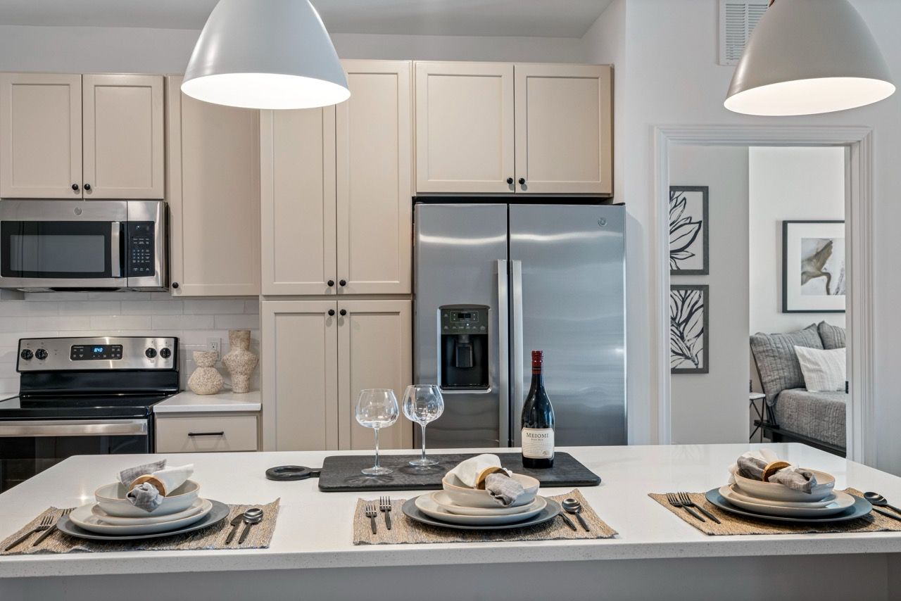 Modern apartment kitchen with stainless steel fridge, microwave, range, and white cabinetry.