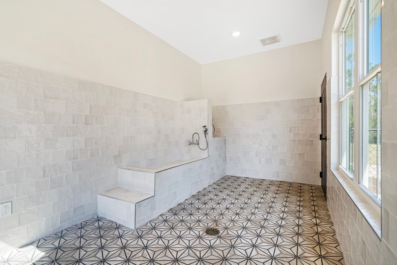 Bright bathroom with white tile walls, a built-in tub on steps, and a large window.