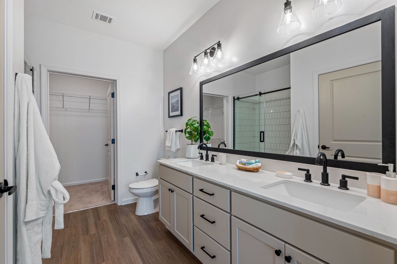 Bright bathroom with a dual-sink vanity, large framed mirror, and a glass-enclosed shower.