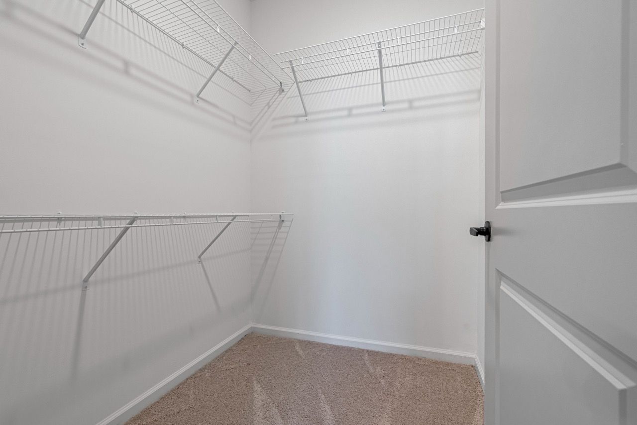 Open walk-in closet with white wire shelving and beige carpet.