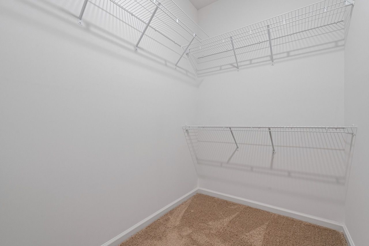 Walk-in closet with white wire shelving on two walls and beige carpet.