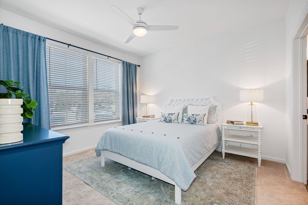 Bedroom in an apartment with white furniture, blue bedding, and blue curtains.