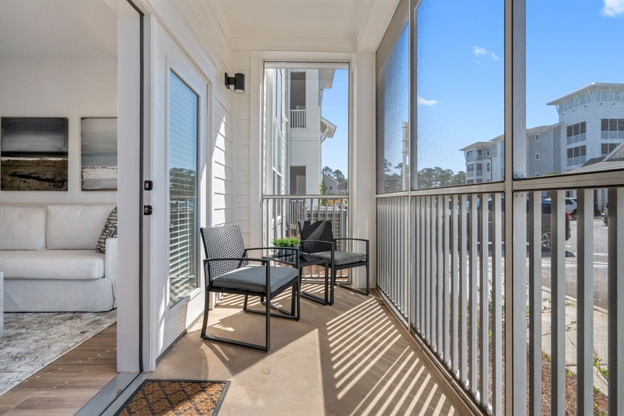 Covered balcony with two chairs and a small plant, visible from living room with sliding doors.