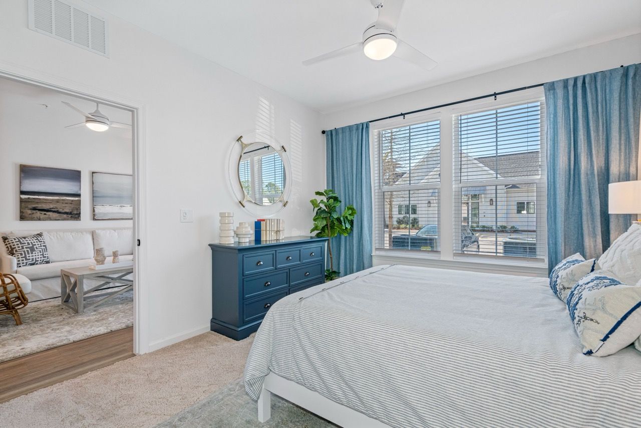 Bedroom in a modern apartment with a bed, dresser, mirror, and a large window.