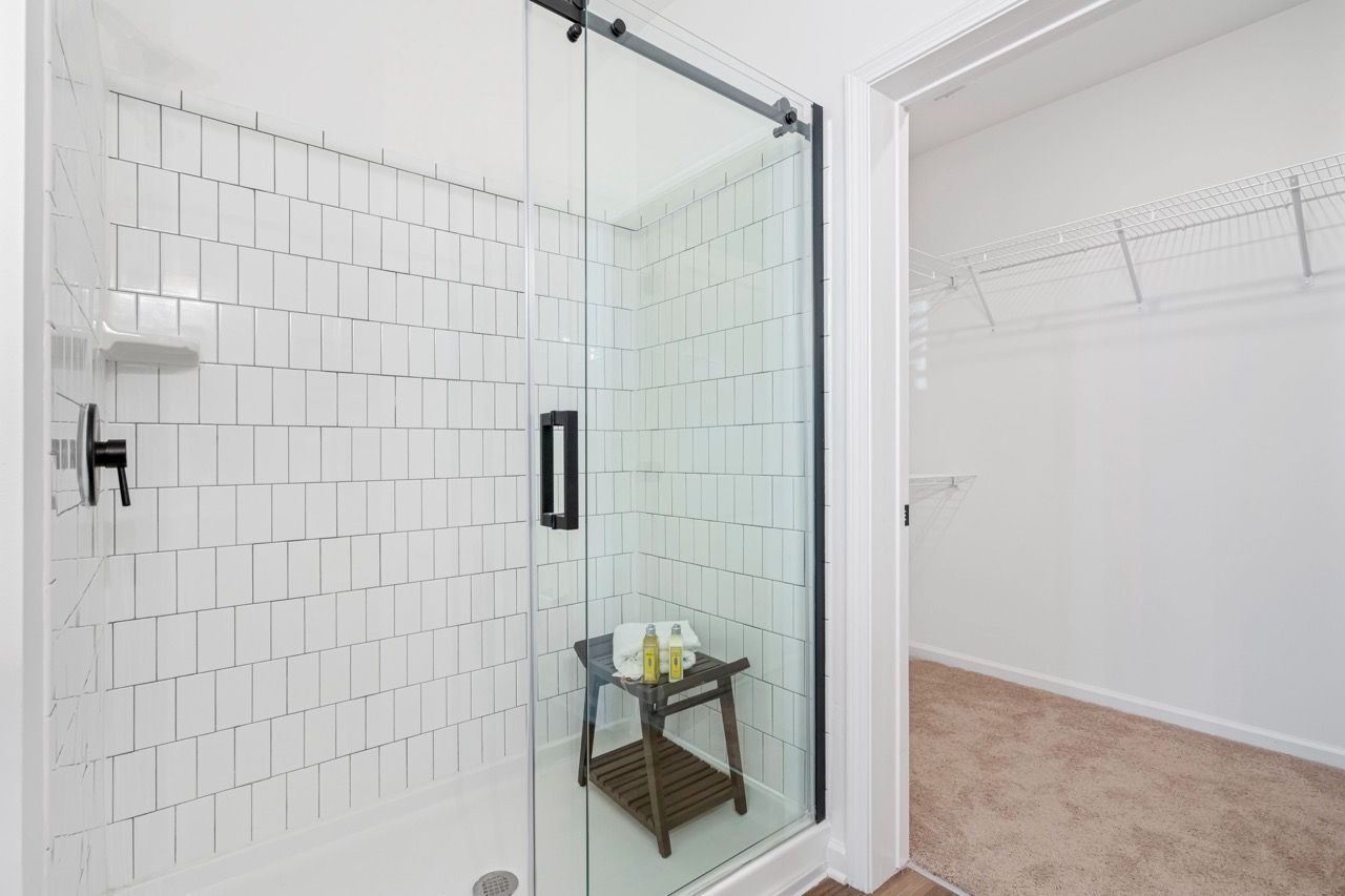 Glass shower enclosure with white subway tile walls and a small wooden stool with toiletries.