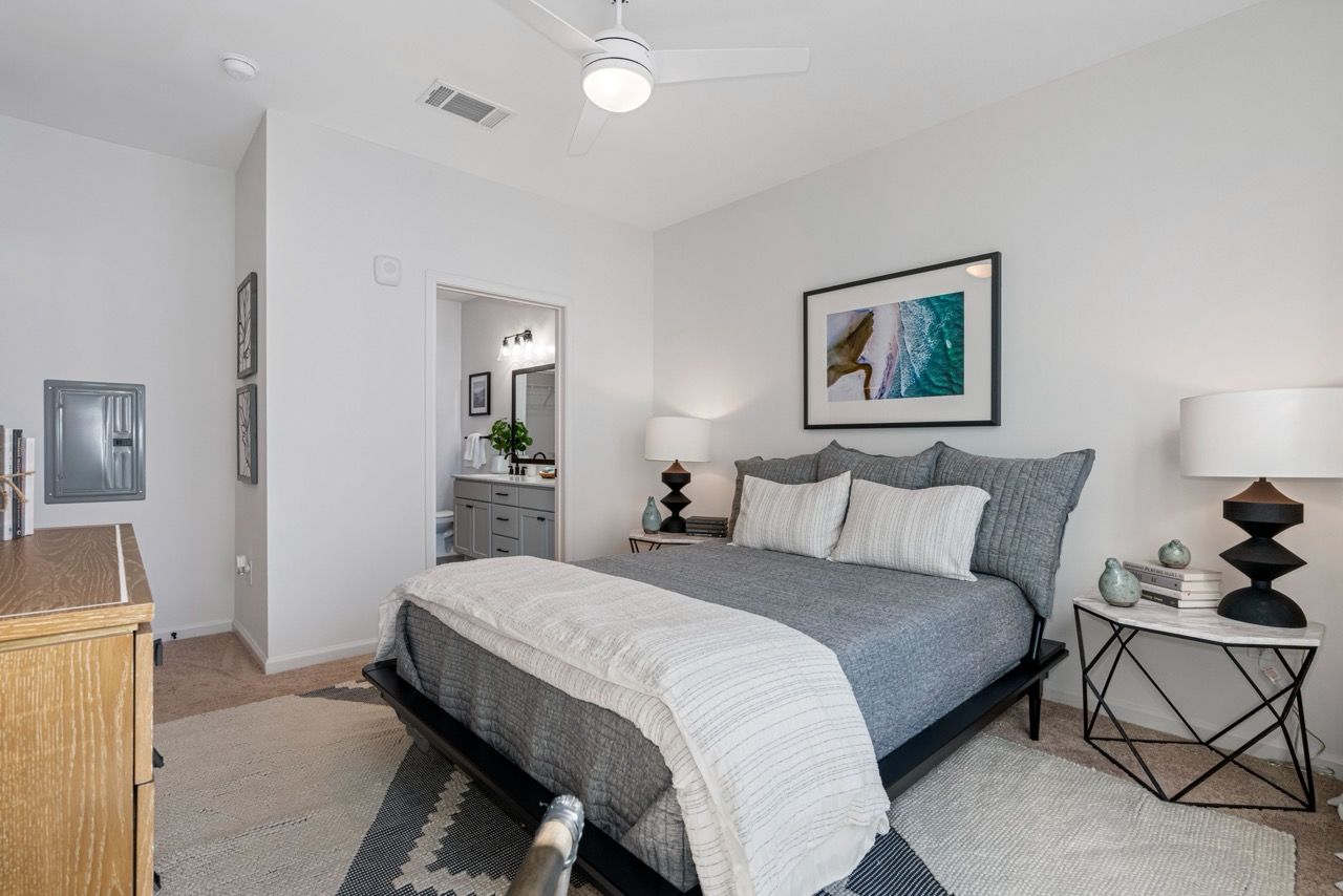 Bedroom in a modern apartment with a queen bed, two nightstands, and an open doorway to the bathroom.