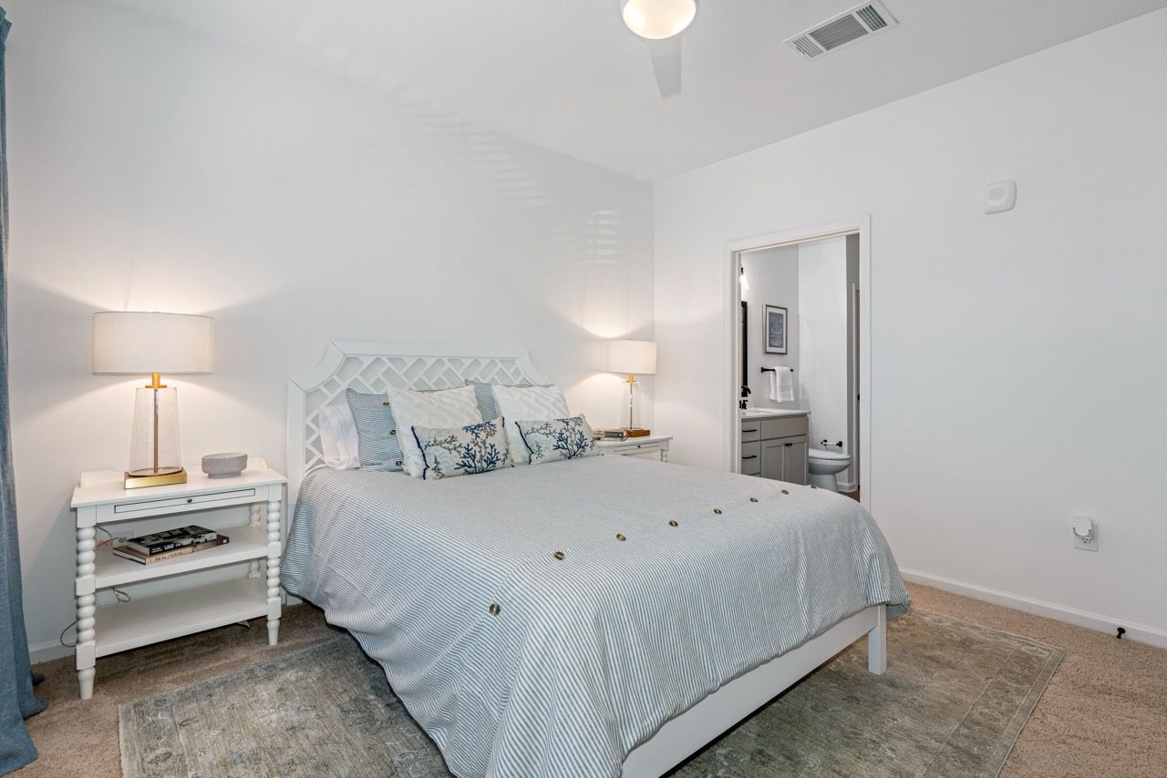 White bedroom with a large bed, two nightstands, and an open door to the ensuite bathroom.