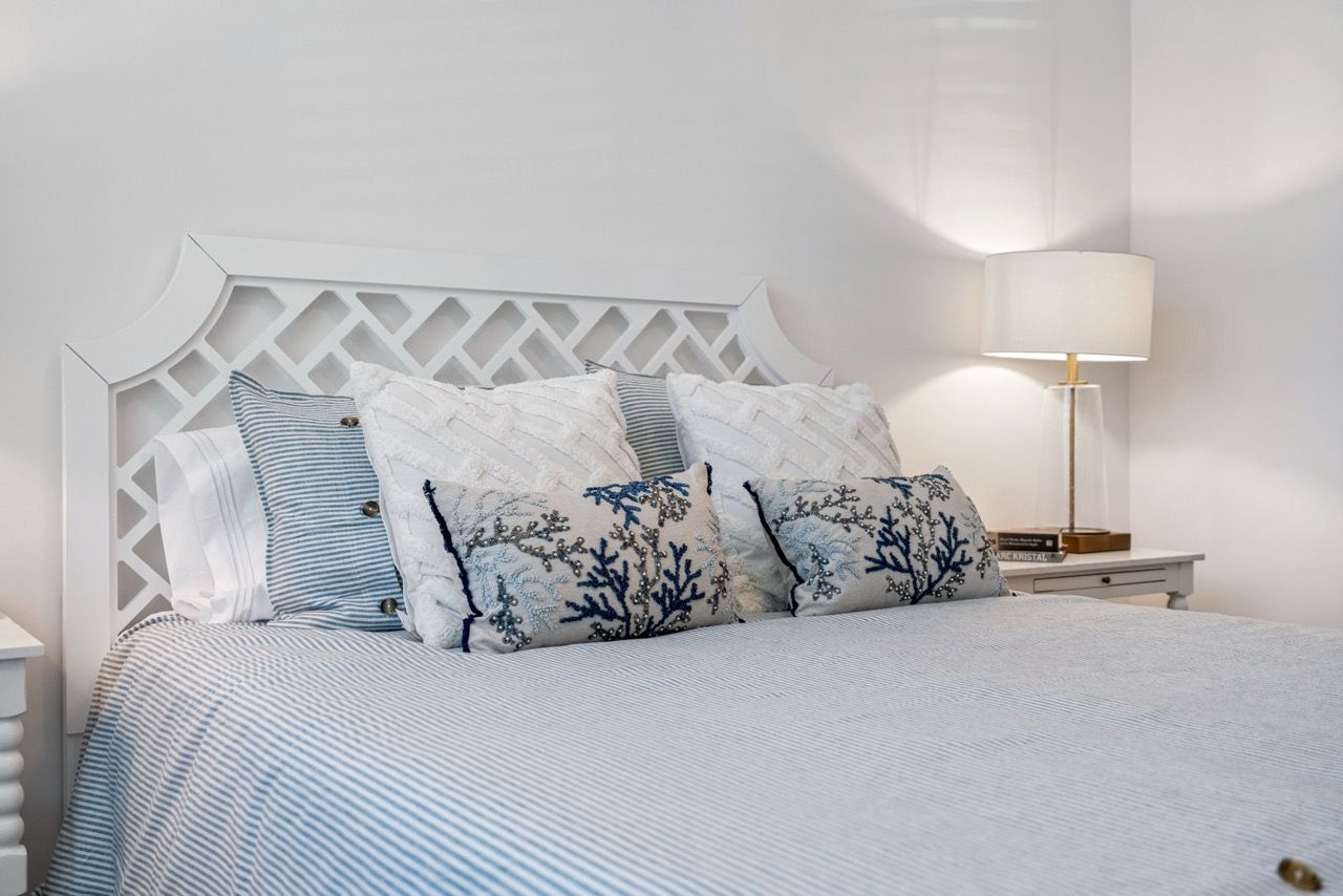 Bedroom with white lattice headboard, blue striped bedding, and decorative pillows beside a lamp.