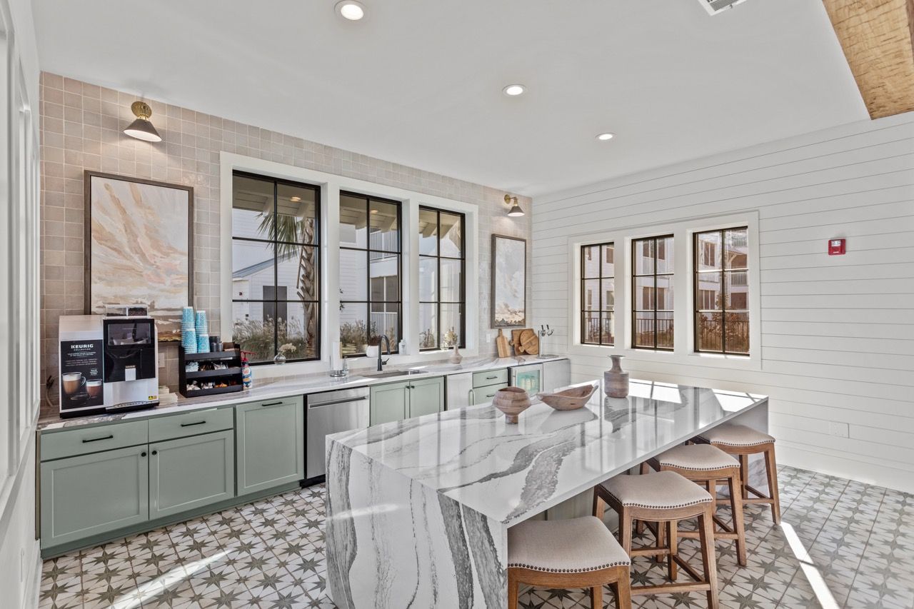 Bright kitchen with marble island, mint-green cabinets, and large windows.