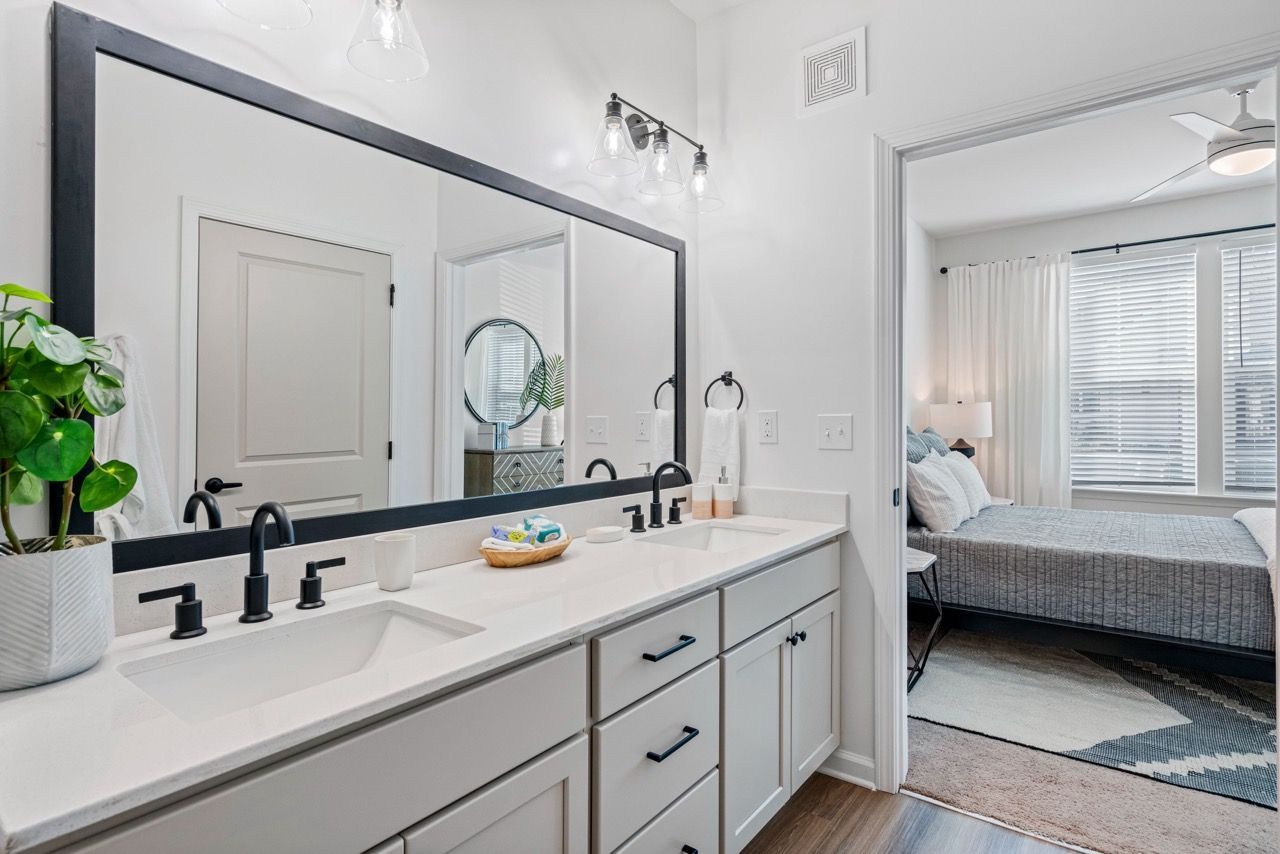 Double-sink bathroom vanity with a large mirror, adjacent to a bedroom.