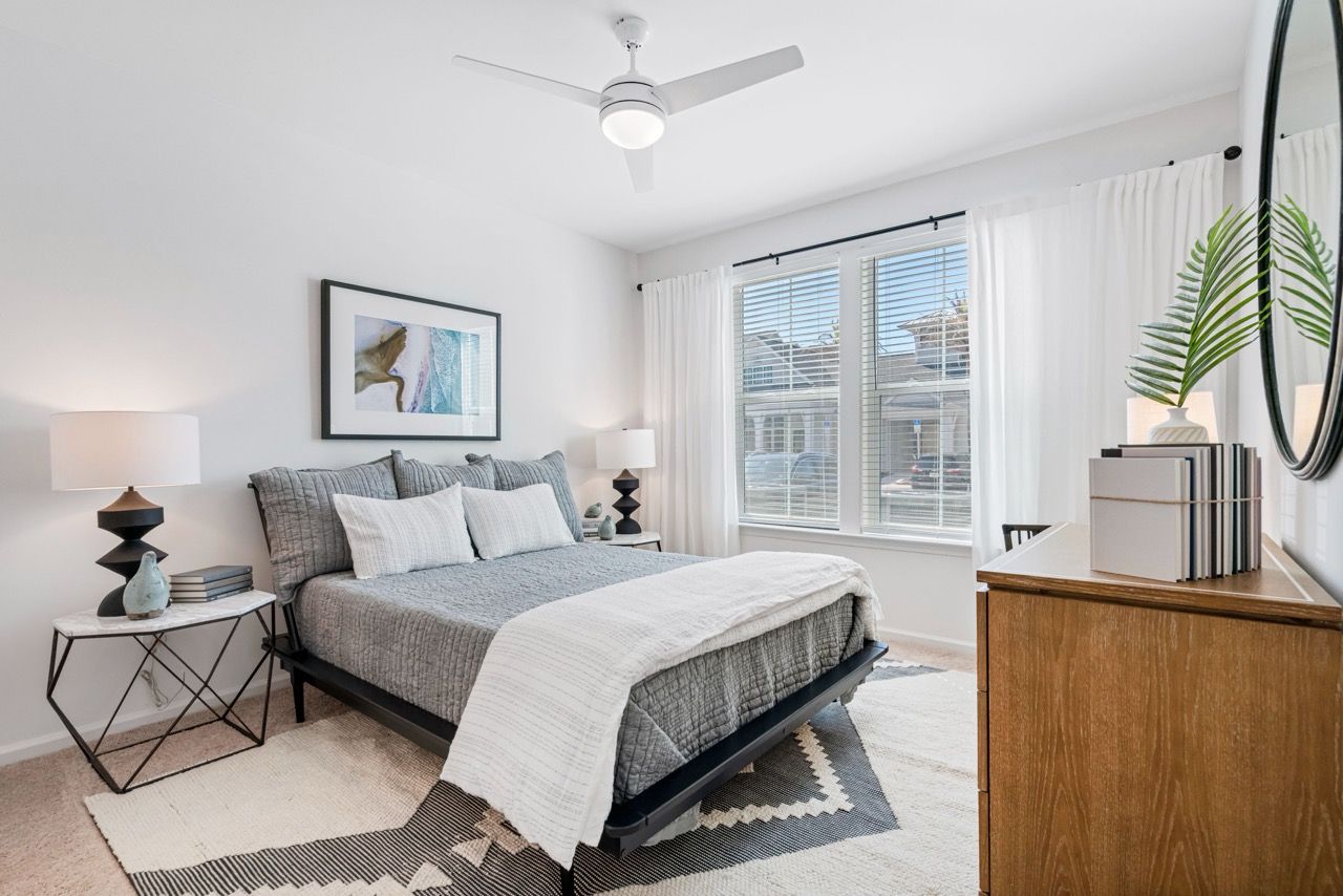 Bedroom in a modern apartment with a bed, two nightstands, dresser, and a large window.
