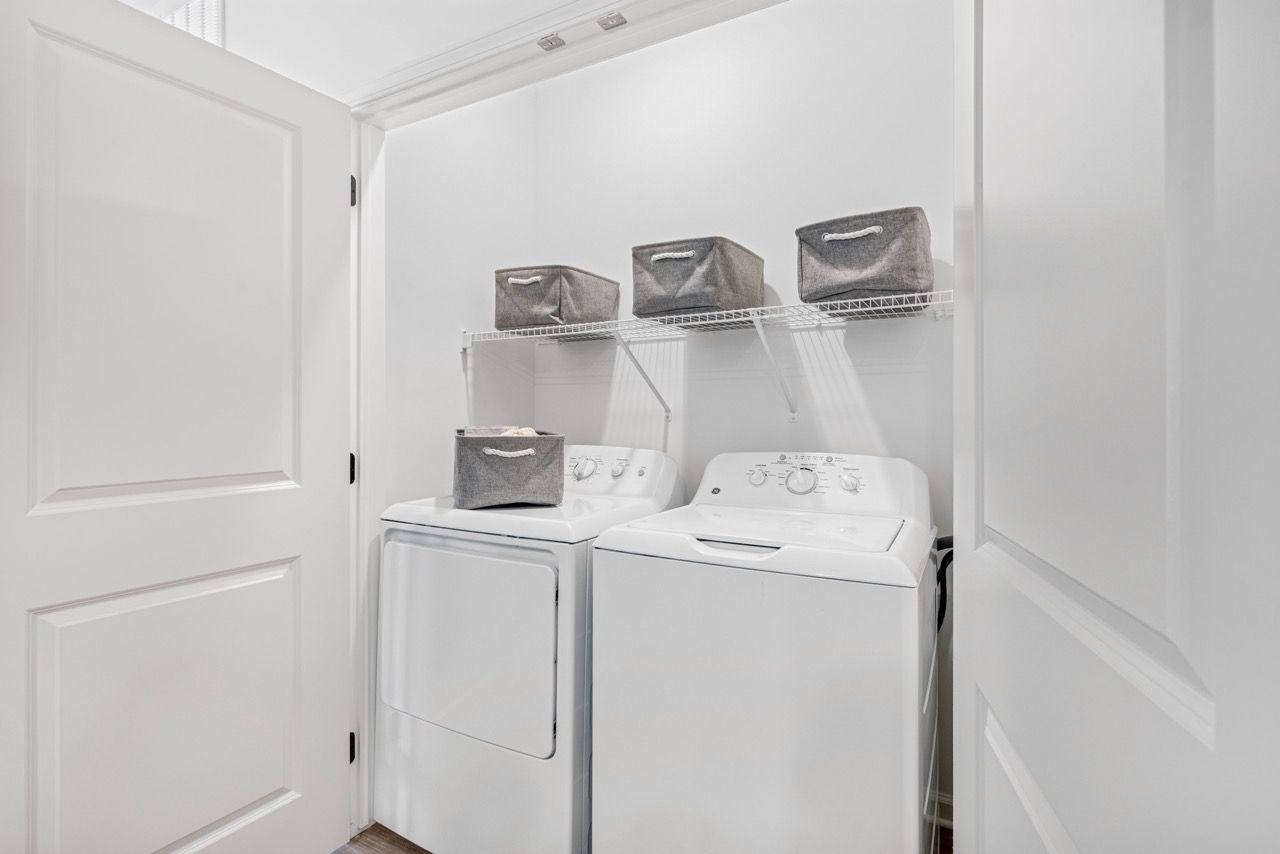 Laundry closet with a washer and dryer side by side and wire shelving with gray storage bins.
