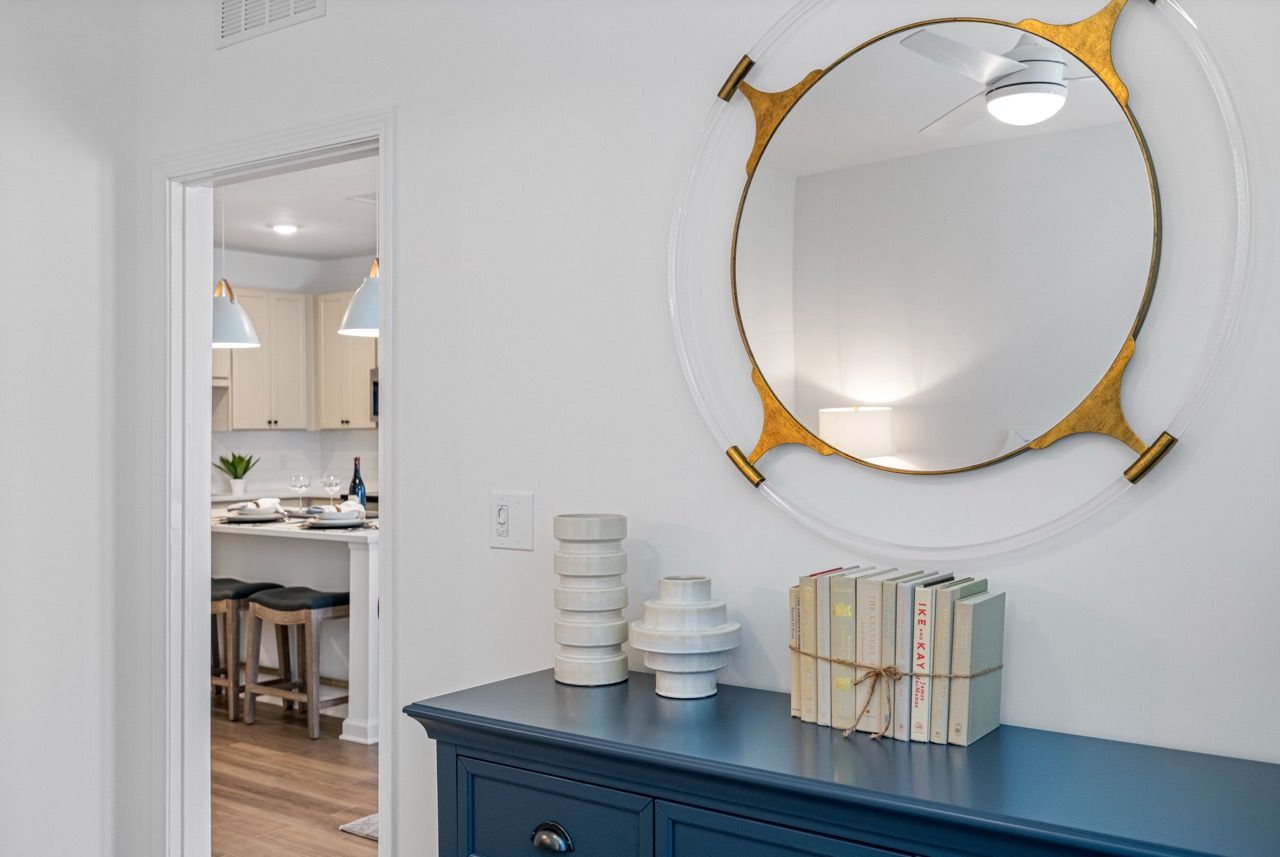 Interior hallway with blue console table, round mirror, and a view into a kitchen with bar stools.