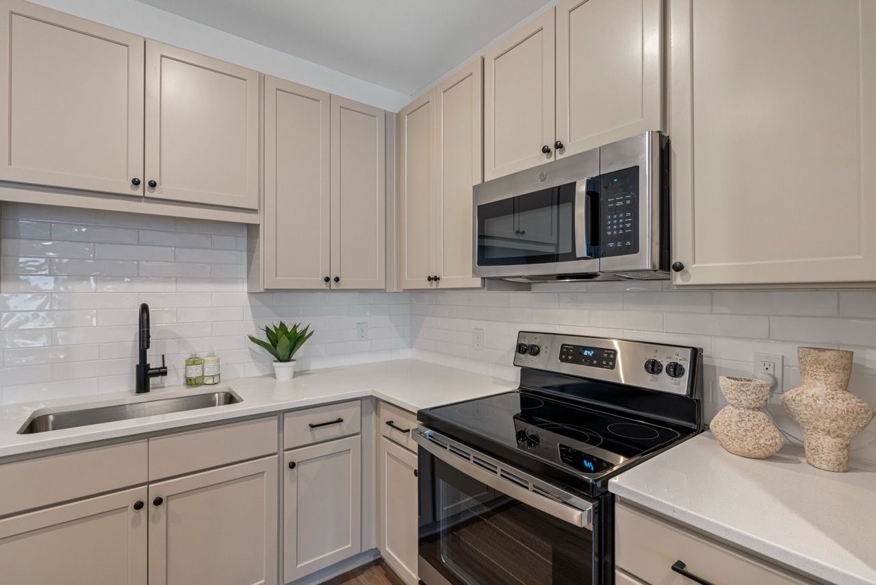 Modern beige kitchen in apartment with white countertops and stainless steel appliances.
