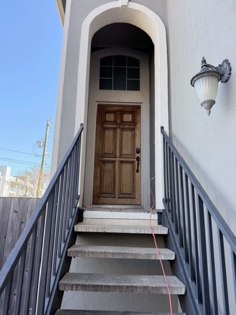 A front entrance with stone steps leading up to an arched wooden door, flanked by dark railings and an outdoor lamp.