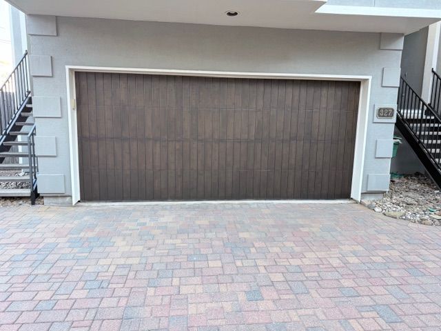A dark wood-toned garage door set in a light grey building with a stone-paved driveway.