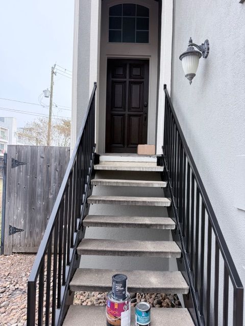 Concrete stairs with black metal railings lead to a dark brown front door; paint cans sit on the bottom step.