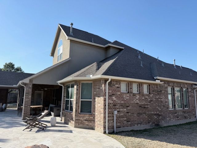 A two-story house with a brick exterior, stone patio, and gabled roof under a clear blue sky.