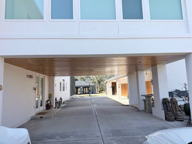 A ground-level view of a modern building with a covered concrete driveway, wood-paneled ceiling, and large frosted windows.