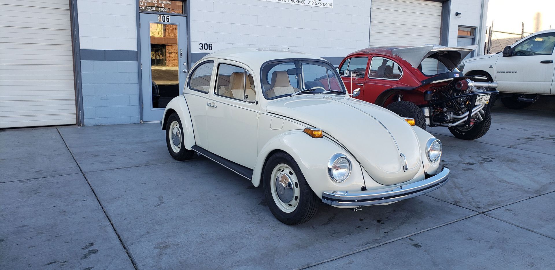 A white volkswagen beetle is parked in front of a garage.
