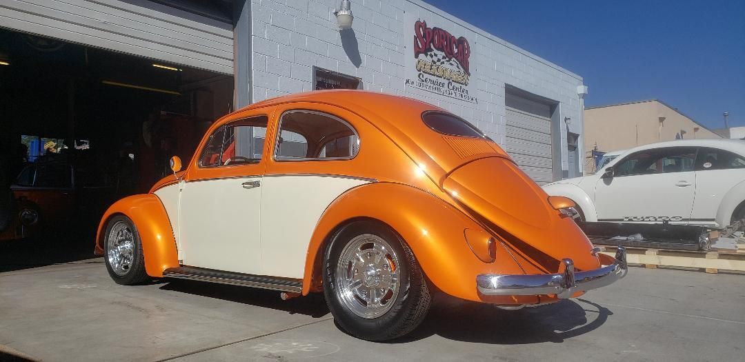 An orange and white volkswagen beetle is parked in front of a garage.
