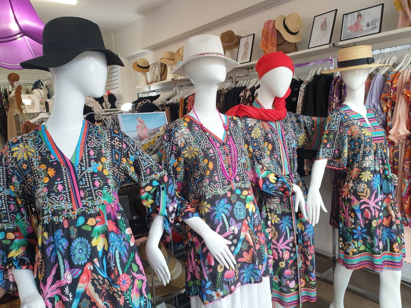 Four mannequins wearing colorful floral print tunics, hats, in a boutique setting.