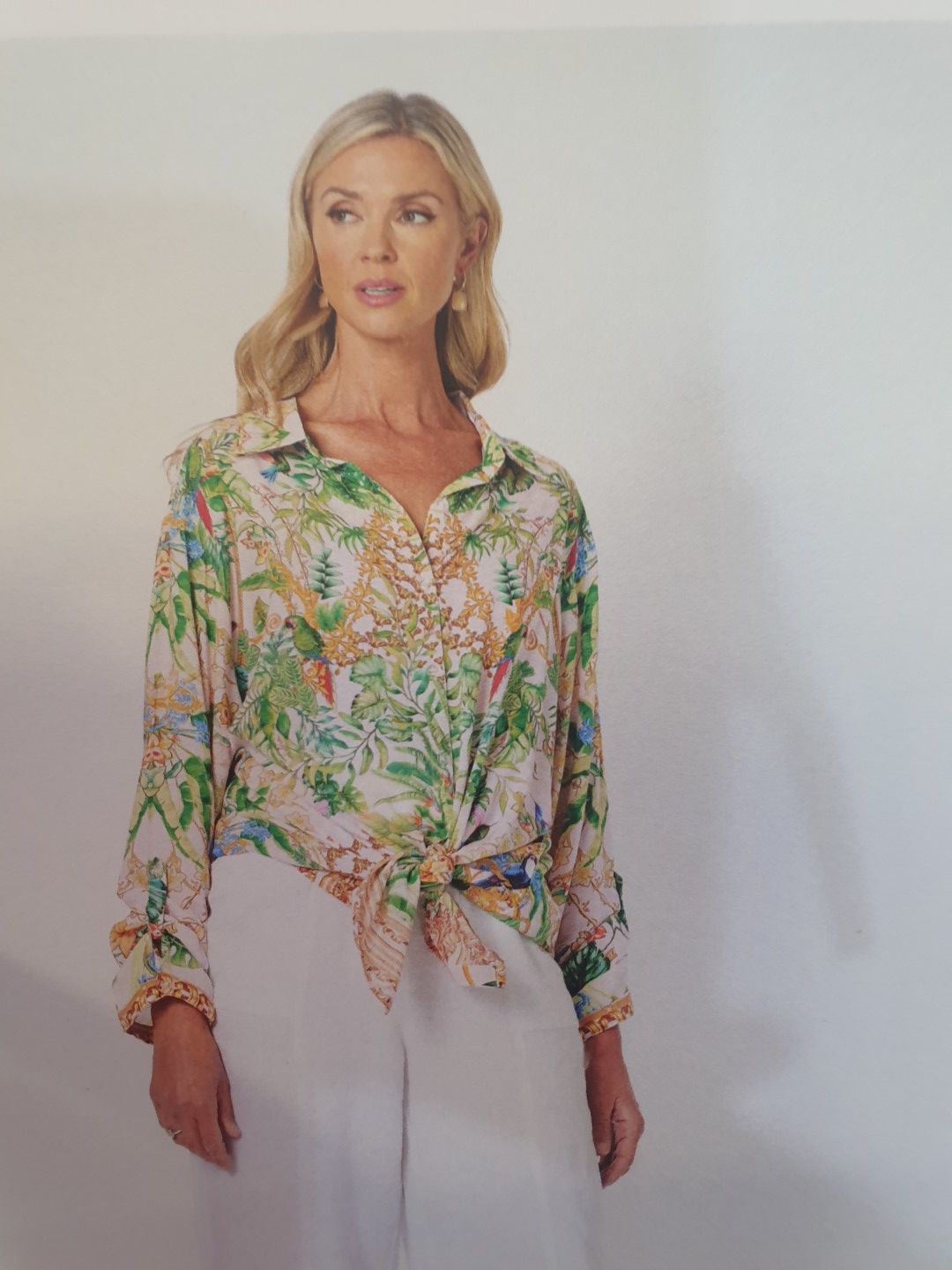 Woman in printed shirt tied at waist, wearing white pants.