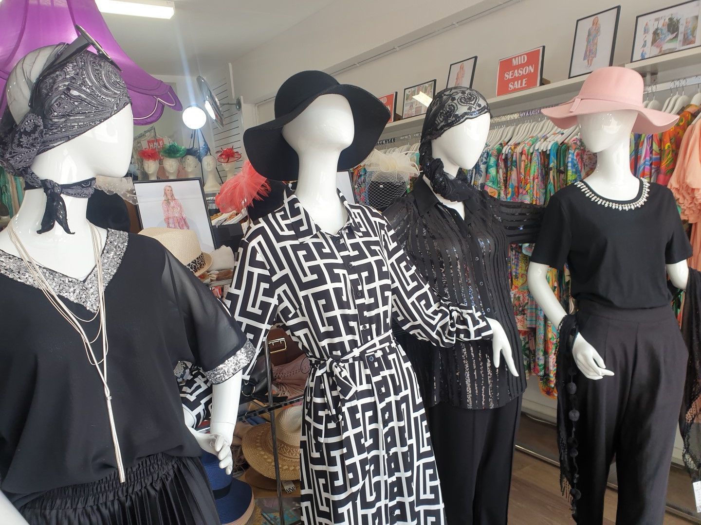Four mannequins in a boutique wearing black and patterned outfits, hats, and scarves; a shopping environment.