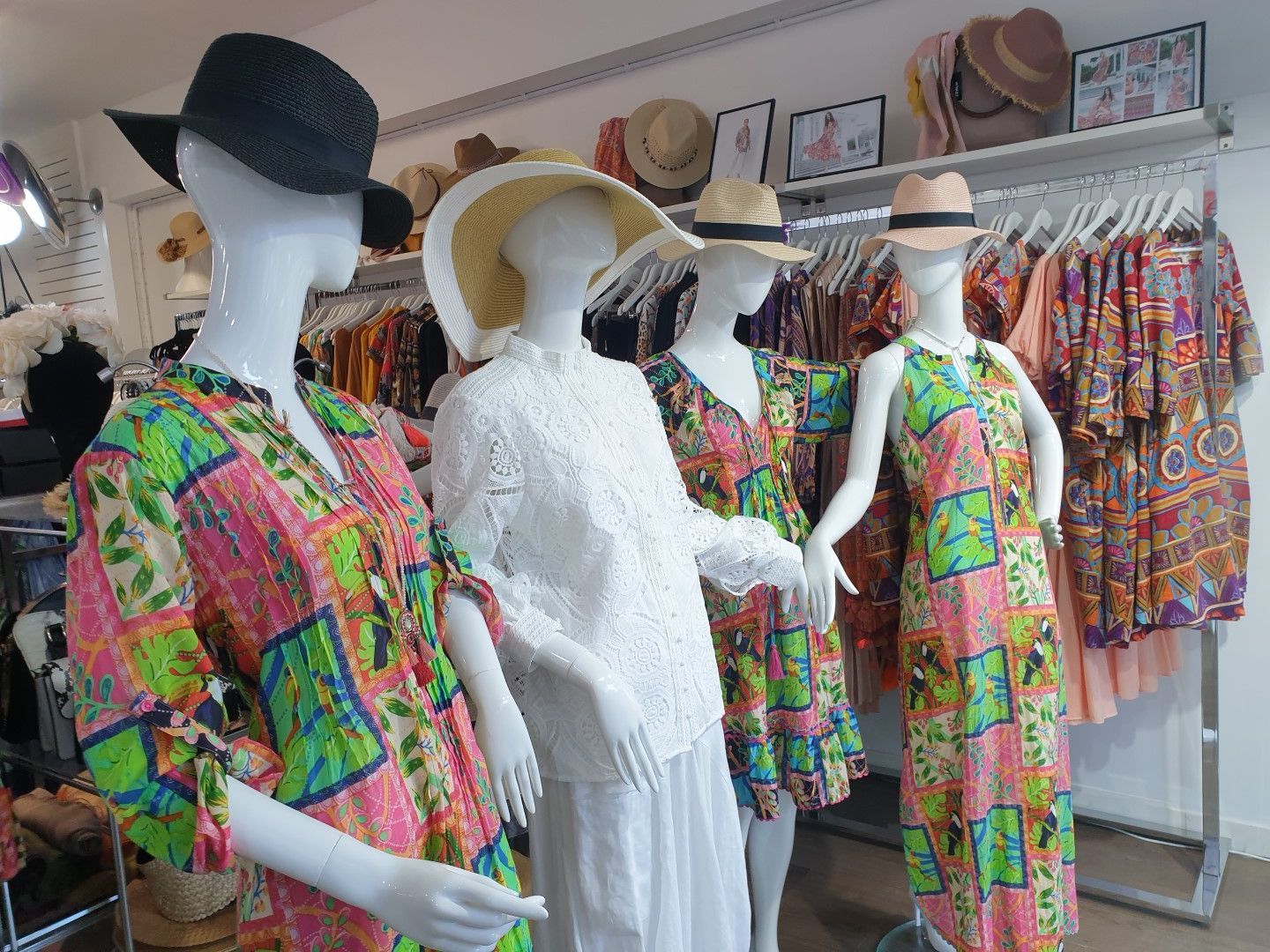 Mannequins in a shop display colorful summer dresses and hats.