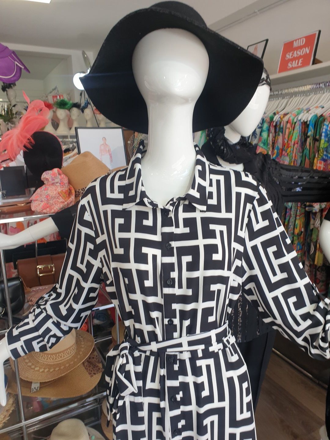 Mannequin in a black and white patterned dress and black hat in a clothing store.