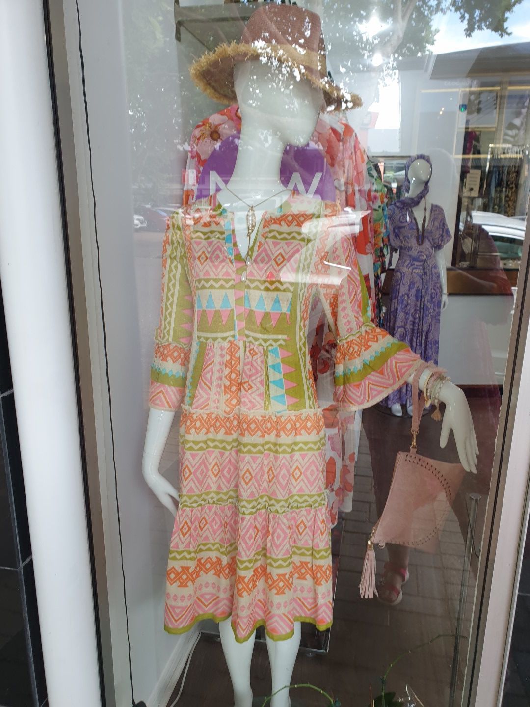 Mannequin in a patterned, colorful dress, hat, and purse in a shop window.