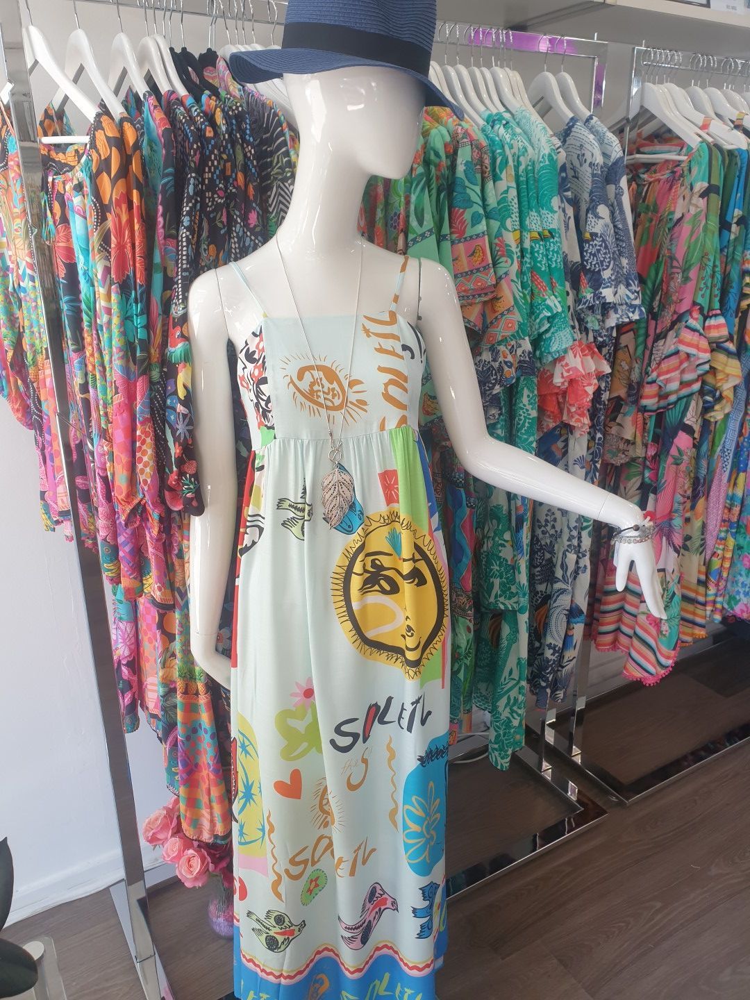 Mannequin wearing a light blue sundress with colorful print, blue hat, in clothing store.