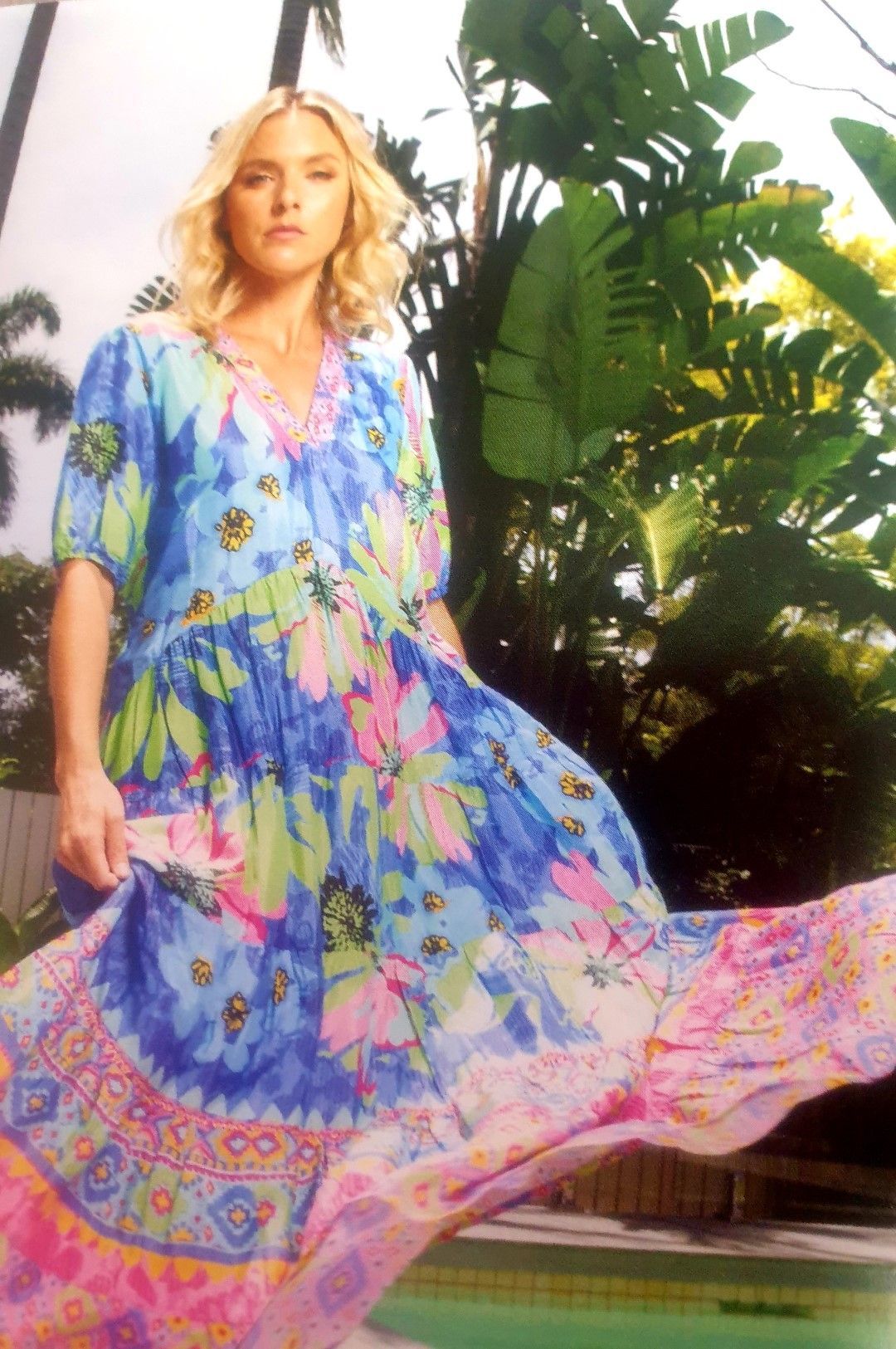 Woman in flowing, patterned dress in a tropical setting.