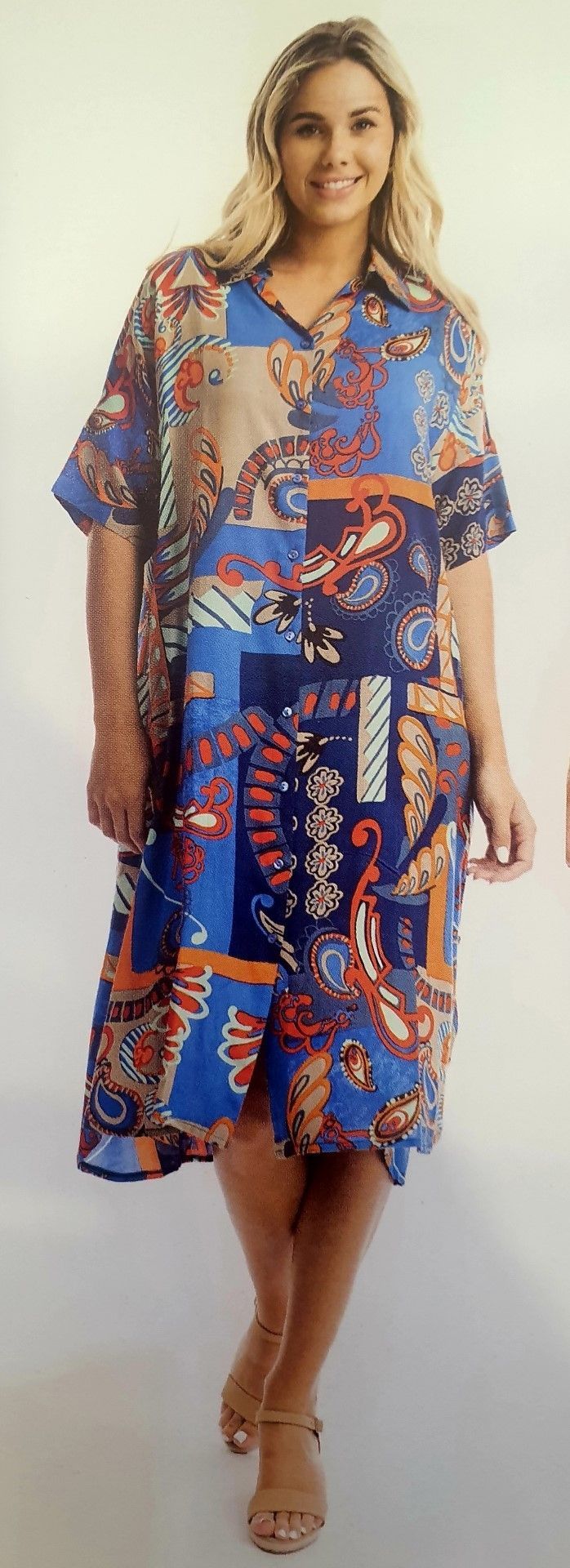 Woman wearing a patterned blue dress and sandals, smiling and standing in front of a white background.