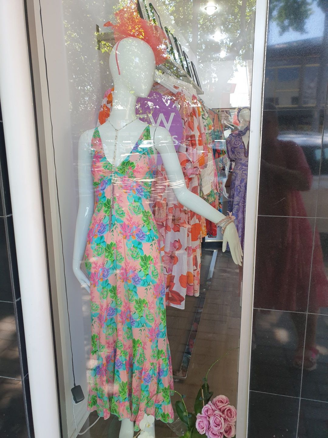 Mannequin in floral dress in shop window; other dresses visible.