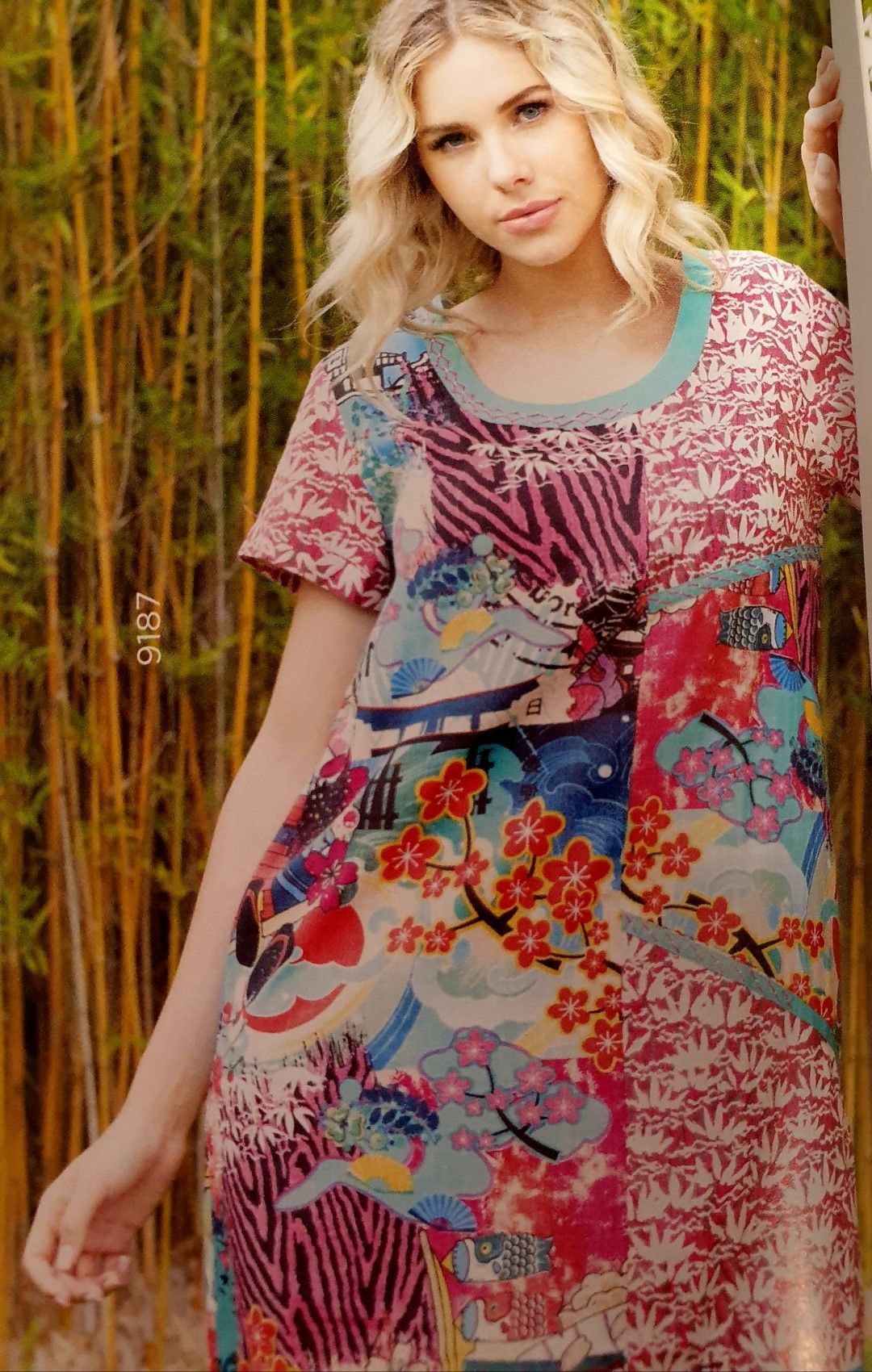 Woman in patterned dress outdoors with bamboo, looking at the camera.