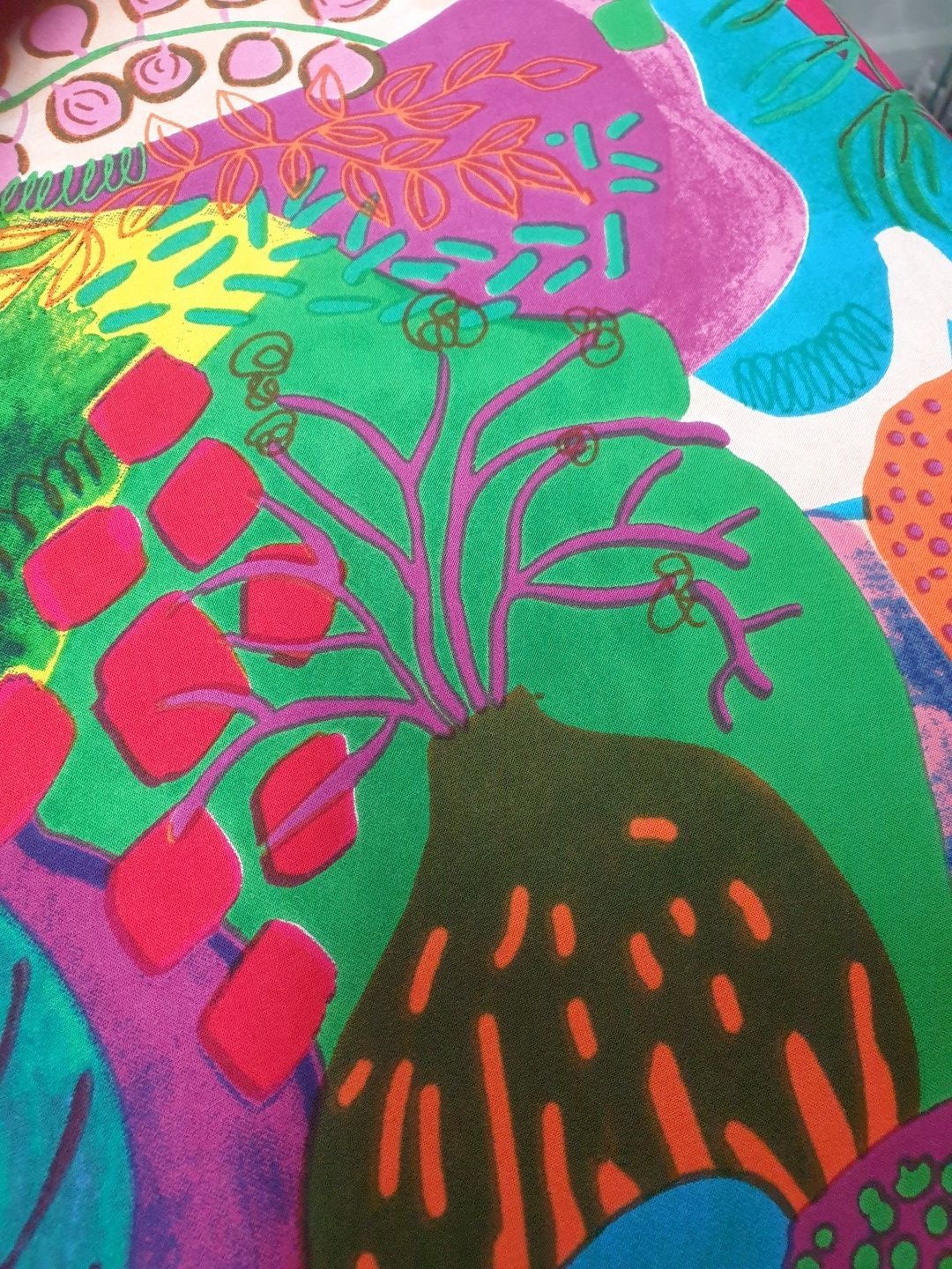 Abstract textile with colorful organic shapes, including red, green, purple, and orange.