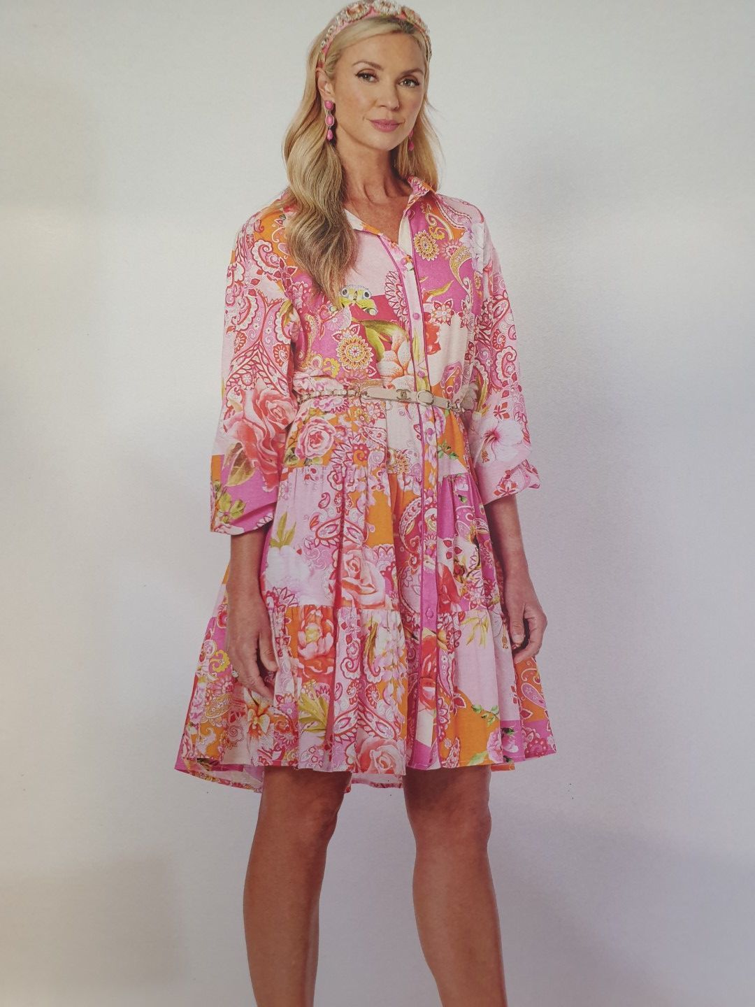 Woman in pink floral dress, standing against a plain background.