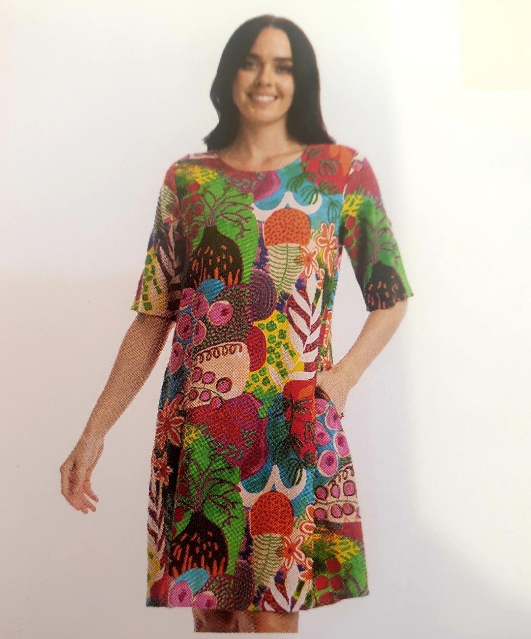 Woman in a colorful printed dress with a round neck, short sleeves, and pockets, smiling.