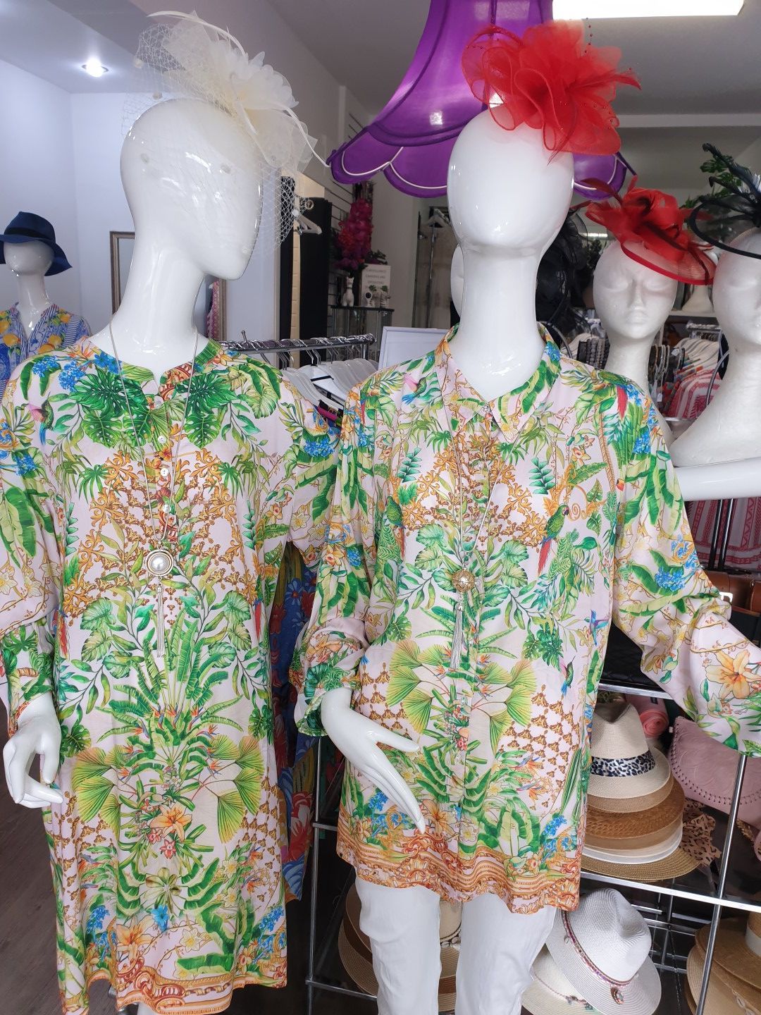 Two mannequins wearing floral shirts and hats in a shop.