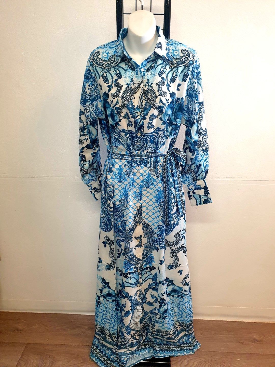 Blue and white patterned dress on a mannequin, belted at the waist, on a stand.